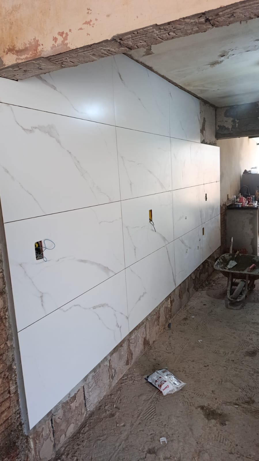 parede recém revestida com porcelanato branco marmorizado em obra ainda em acabamento, com betoneira e saco de