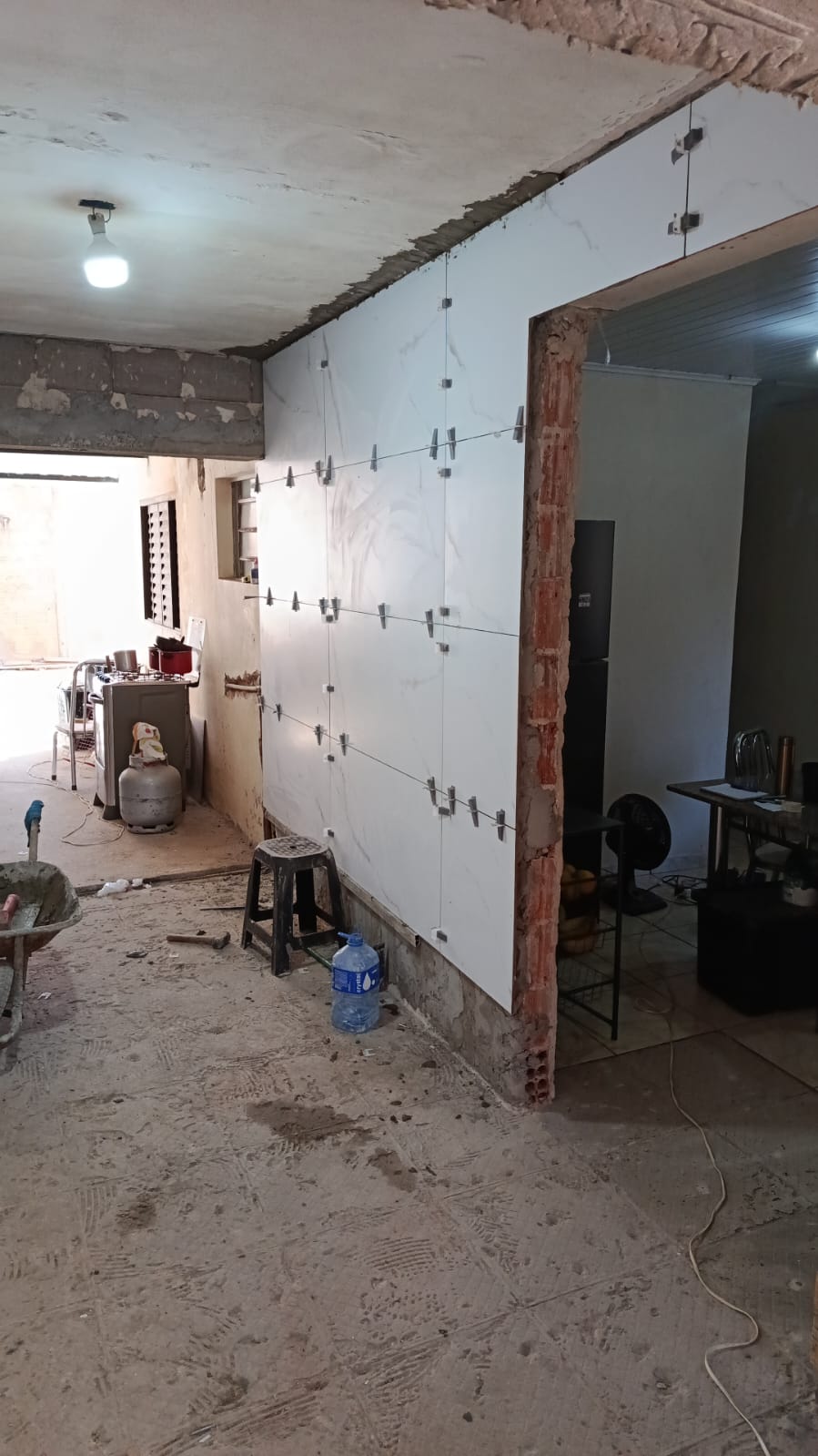 obra de reforma residencial com parede de porcelanato branco sendo instalada com niveladores, ao lado de uma c